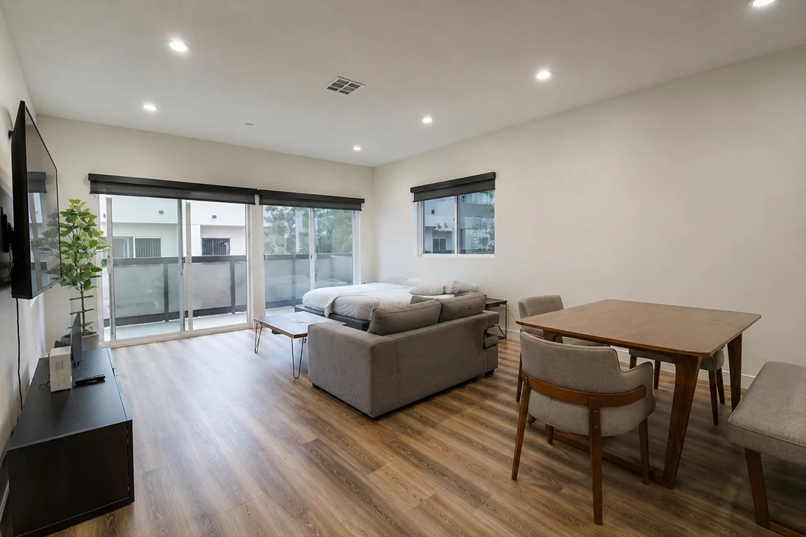 Basic Airbnb studio apartment before interior transformation, with plain white walls, sofa bed, dining table, minimal decor, cold ceiling lights and unused visual potential.